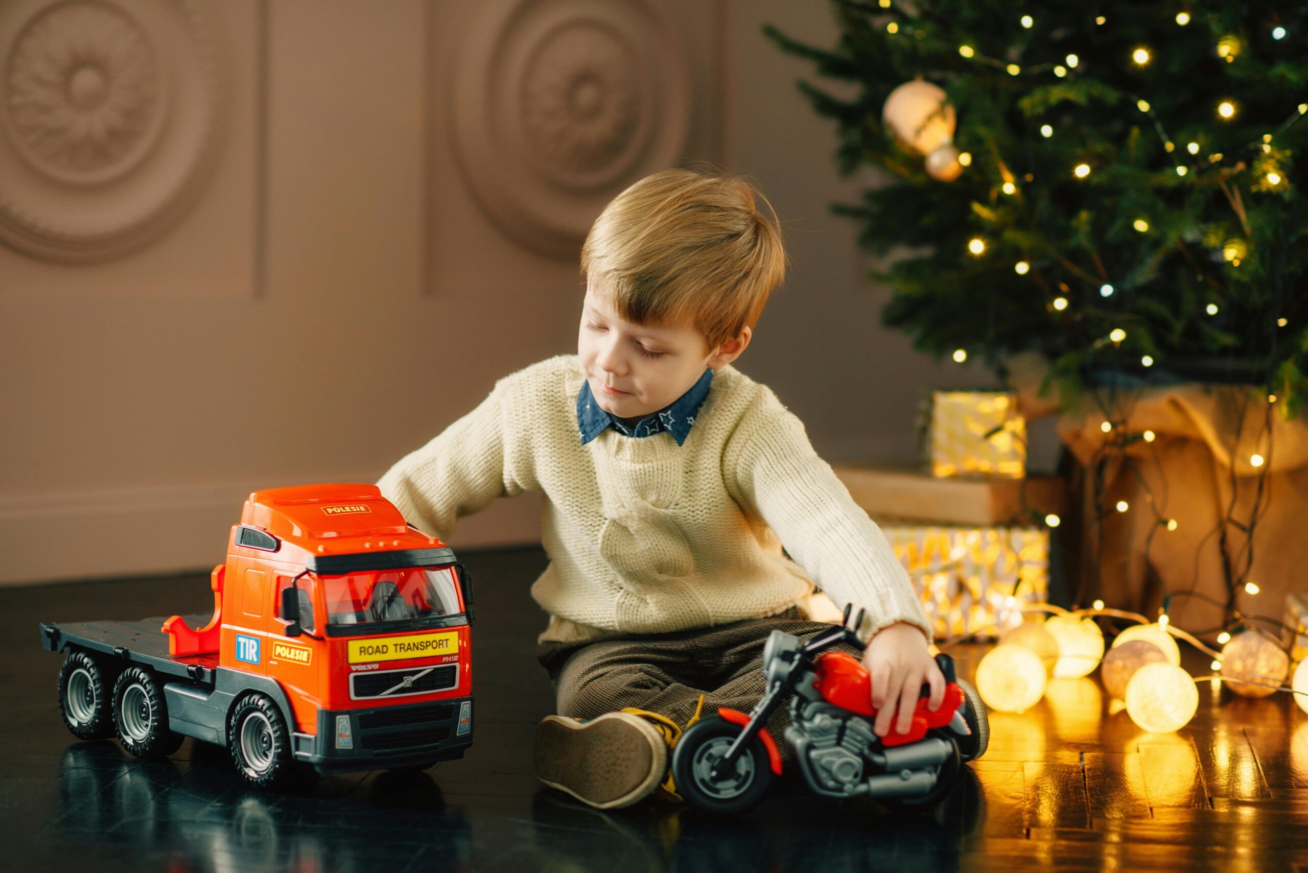 A young child enjoys playtime with toys near a festive Christmas tree.